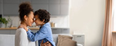 Afrika kökenli Amerikalı anne sıcak, samimi bir anda oğlunu kucaklıyor. Neşeli bir bağı ve bağı paylaşan güneş ışığı pencerelerden akar..