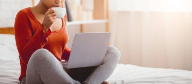 Tanımlanamayan afro kadın dizüstü bilgisayar kullanıyor hafta sonu sabahı evde yatağında kahve içiyor. Panorama, Kırpılmış, Boş Alan