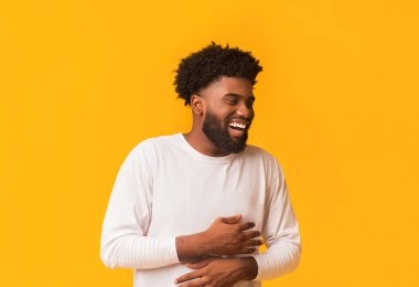 Genç Afrikalı Amerikalı komik adam kahkahalarla gülüyor, komik fıkralar duyuyor, karın kaslarında ağrı hissediyor kıkırdama, turuncu stüdyo arka planı, kopyalama alanı