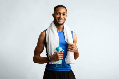 Susuz kalma. Boynunda havluyla, elinde maden suyu şişesi olan, kameraya gülümseyen kaslı afro adam.