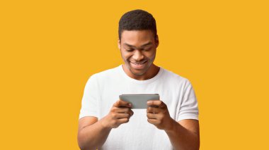 Modern Jenerasyon. Portakal duvarı, telif alanı, panorama üzerinden cep telefonuyla cep telefonu oyunu oynayan Afrikalı bir adam.