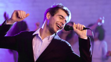 Karaoke Partisi. Şarkı söyleyen genç adam mikrofon tutuyor ve arkadaşlarıyla gece kulübünde eğleniyor. Panorama, Mavi Işık