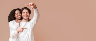 Mutlu anları yakalıyorum. Romantik ırklar arası çift elleriyle çerçeve yapıyor ve sarı arka planda sarılıyorlar, boşluğu kopyala