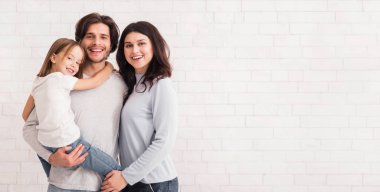 Mükemmel aile. Mutlu anne, baba ve onların sevimli küçük kızının portresi beyaz tuğla duvarın arkasında dikiliyordu.