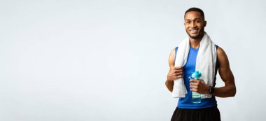 Susuz kalma. Boynunda havluyla, elinde maden suyu şişesi olan, kameraya gülümseyen kaslı afro adam.