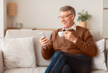 Mutlu kıdemli beyefendiler akıllı telefon mesajları atıyor ve evdeki koltukta kahve içiyor. Seçici Odaklanma
