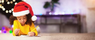 Noel Baba 'ya mektup. Afrikalı çocuk dilek listesi yazıyor, Noel ağacının yanında yerde yatıyor.