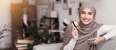 Çevrimiçi bankacılık. Akıllı telefon ve kredi kartıyla tesettürde oturan mutlu Arap kadın portresi ödemeler için yeni uygulamanın keyfini çıkarıyor.