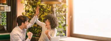 İki çok ırklı meslektaşı heyecanlarını dile getiriyor ve başarılarını yeşillik ve kopyalama alanlarıyla süslenmiş şık bir çalışma alanında beşlikle kutluyorlar.