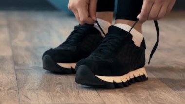 Bir insan ahşap bir zeminde otururken parlak siyah spor ayakkabılarının bağcıklarını ayarlıyor. Odak noktası ayakkabı tasarımı, aktif bir yaşam tarzı ve detaylara dikkat etmek..