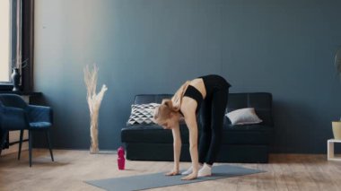 Bir kadın büyük pencereli şık bir oturma odasında yoga pozu veriyor. Mekanda minimalist bir tasarım ve yumuşak doğal ışık var. Pratik için sakin bir atmosfer yaratıyor..