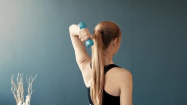 Uzun saçlı bir kadın yoga stüdyosunda kolunu yukarı doğru uzatıyor. Sakinleştirici mavi arka plan, sakin atmosferi güçlendirir, rahatlamasını sağlar ve alıştırması sırasında odaklanmasını sağlar..