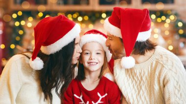 Hayaller gerçek olur. Noel arifesinde Noel Baba şapkalı ebeveynler mutlu kızı öpüyor, küçük kız büyük güzel bir hediye tutuyor, mutfak içi.