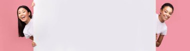 İki Afro ve Asyalı kız, boş beyaz panodan Pembe Stüdyo 'nun arka planında kameraya gülümsüyor. Panorama