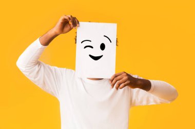 Turuncu arka planda pozitif emojisi olan siyah bir adam gerçek duygularını saklıyor.