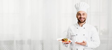 Şef yemek servisi yapıyor. Mutfakta duran kameraya gülümseyen tavuklu mutlu aşçı tabağı. Seçici Odaklanma