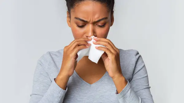 stock image Black girl touching her nose with napkin, having runny nose, grey background