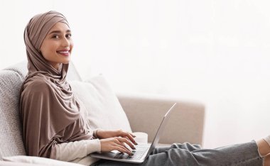 Çevrimiçi Derece Kavramı. tesettürde gülümseyen müslüman kız evde dizüstü bilgisayar kullanıyor, internette okuyor, yabancı diller öğreniyor, yan görünüm, kopyalama alanı