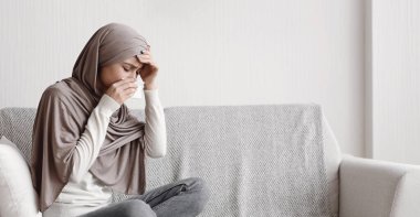 Grip ve Soğuk Konsepti. Sıcak ve akışkan burundan muzdarip hasta Müslüman kız, evinde koltukta otururken kendini iyi hissetmiyor, boşluğu kopyalıyor.
