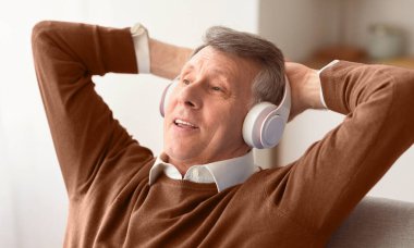 Kulaklıklı gevşemiş son sınıf öğrencisi evde koltukta oturmuş müzik dinlerken el ele tutuşuyor. Seçici Odaklanma