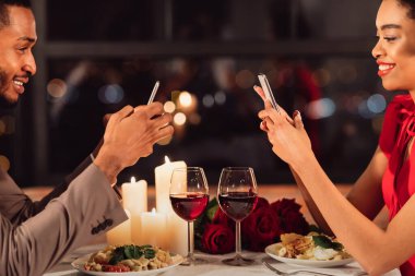 Online Randevu Uygulaması. Şık Restoranda romantik bir akşam yemeği sırasında cep telefonu kullanan neşeli çift. Kırpılmış