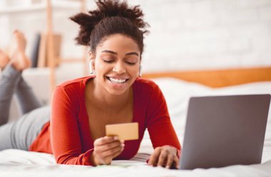 Çevrimiçi bankacılık. Hafta sonları evde yatağında yatan kredi kartı ve dizüstü bilgisayar kullanan siyahi bir müşteri. Seçici Odaklanma