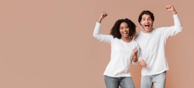 Yes. Overjoyed interracial couple celebrating success with raised fists, posing together over yellow background with empty space