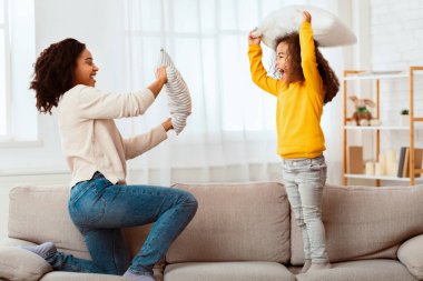 Aile eğlencesi. Afro anne ve kızı evde yastık savaşı yaparken mutlu. Seçici Odaklanma