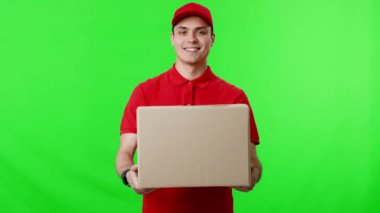 Kırmızı üniformalı neşeli bir teslimatçı, parlak yeşil bir zemin üzerine kurulmuş bir karton kutuyu sunar. Bu da o ana enerji katar..