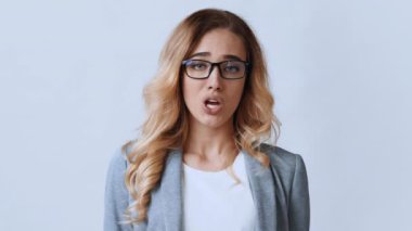 Uzun, dalgalı saçlı genç bir kadın parlak bir ofis alanında açık gri bir ceket giyerken kendinden emin bir şekilde konuşur. Çevre profesyonel ve modern bir iş yeri ortamı öneriyor.