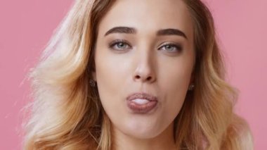 Dalgalı saçlı genç bir kadın sakızıyla büyük bir balon şişiriyor. Çekim için poz verirken rahat bir yüz ifadesi var, canlı pembe bir arka plana karşı neşeli tarafını gösteriyor..