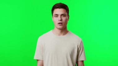 Genç bir adam, yüzünde sıkılmış bir ifadeyle canlı yeşil bir altyapının önünde duruyor.