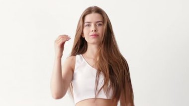 Uzun saçlı, kendine güvenen genç bir kadın temiz, minimalist bir stüdyoda şık bir tek omuzlu bluz giyerken nazikçe saçlarını savuruyor. Parlak arka plan onun zarafetini arttırıyor..