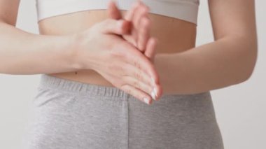 Genç bir kadın oturuyor, iki elini de nazikçe masaj yapmak için kullanıyor. Rahatlamış görünüyor, sakin bir ev ortamı sergiliyor. Yumuşak, doğal bir ışıkla tenini aydınlatıyor..