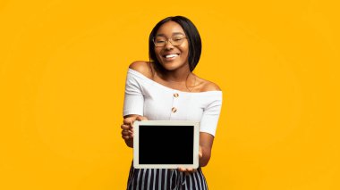 Harika bir uygulama. Gülümseyen Afro Kız, Stüdyoda Portakal Arkaplan Üzerinde Duran Boş Ekran Tabletini Gösteriyor. Panorama, Mockup