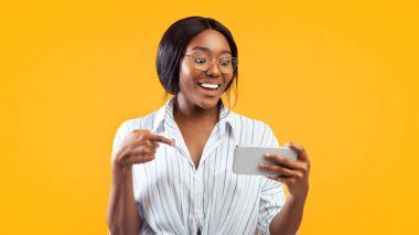 Buraya bak. Cep telefonu tutan afro kız parmağıyla ona işaret ediyor ve Pembe Stüdyo 'nun arka planında gülümsüyor. Panorama