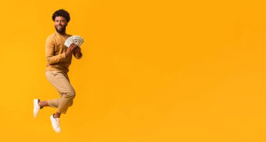 Şanslı günümdeyim. Havaya zıplayan mutlu siyah adam, bir sürü dolar, turuncu arka plan