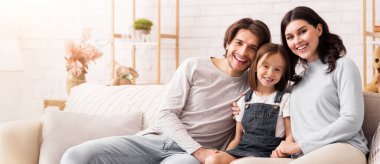 Perfect Family. Portrait of cute little girl posing at camera with her parents, sitting on sofa at home