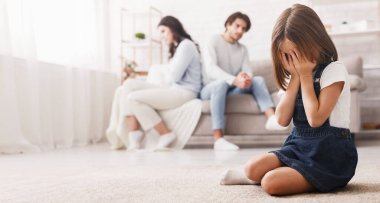 Aile sorunları konsepti. Tartıştıktan sonra anne babasından ayrı oturan ağlayan küçük bir kız. Kavgadan bıkmış, yalnız hisseden bir çocuk.