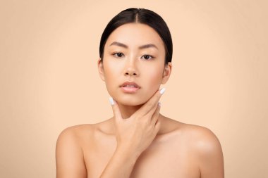 Cilt bakımı özgüven. Tişörtsüz Asyalı Kadın Boynuna Nazikçe Dokunuyor, Doğal Güzelliği Kutluyor, Gri Stüdyo Arkaplanının Üzerindeki Kameraya Bakıyor. Vücut ve Yüz Bakımı Konsepti