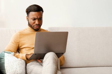 Ciddi bir Afro iş adamı dizüstü bilgisayarda çalışıyor. Evdeki koltukta oturuyor. Boşluğu Kopyala, Seçici Odaklanma