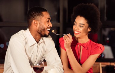 Sevgililer Günü Randevusu. Neşeli Afrikalı Amerikalı çift birbirlerini besliyor. Süslü restoranda romantik bir yemek yiyorlar..