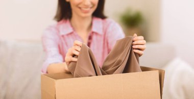 Karton bir kutuda arkadaşına hediye paketi hazırlıyor. Giysileri kutuya koyuyor, kapatıyor, seçici odaklanıyor.