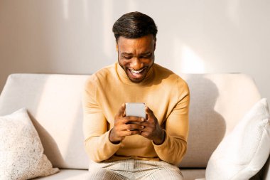 Gezici Oyun. Heyecanlı Afro Adam Cep telefonu kullanıyor Evdeki koltukta oturan oyunlar oynuyor.