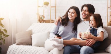 Aile bağı. Mutlu ebeveynler ve küçük kızları evde birlikte televizyon izliyor, patlamış mısır yiyor ve oturma odasında kanepede dinleniyorlar.