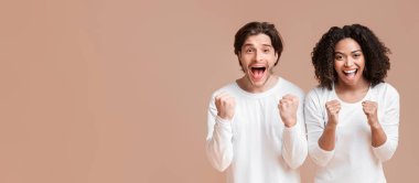 Celebrating Success. Overjoyed Interracial Couple Rejoicing Victory, Raising Clenched Fists In Excitement, Posing Together Over Yellow Background