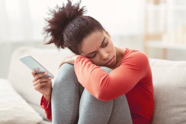 Yalnızlık. Cep telefonu tutan üzgün Afrikalı Amerikalı kadının arayacak arkadaşı yok. Evdeki koltukta oturuyor. Seçici Odaklanma