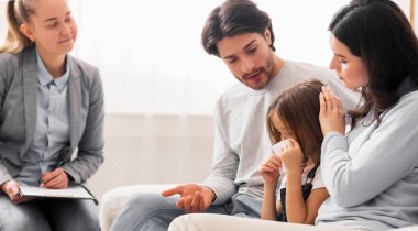 Çocukluk depresyonu kavramı. Çocuk psikologları ofisinde ağlayan küçük kızlarını teselli eden şefkatli ebeveynler.