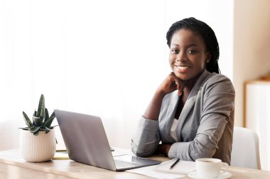 Başarılı bir siyahi iş kadını ofiste oturuyor ve kameraya gülümsüyor, boşluğu kopyalıyor.
