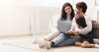Birlikte tatile çıkıyoruz. Genç adam, kadın ve küçük kızları dizüstü bilgisayarı ve kredi kartıyla yerde oturup online rezervasyon yaptırıyorlar.